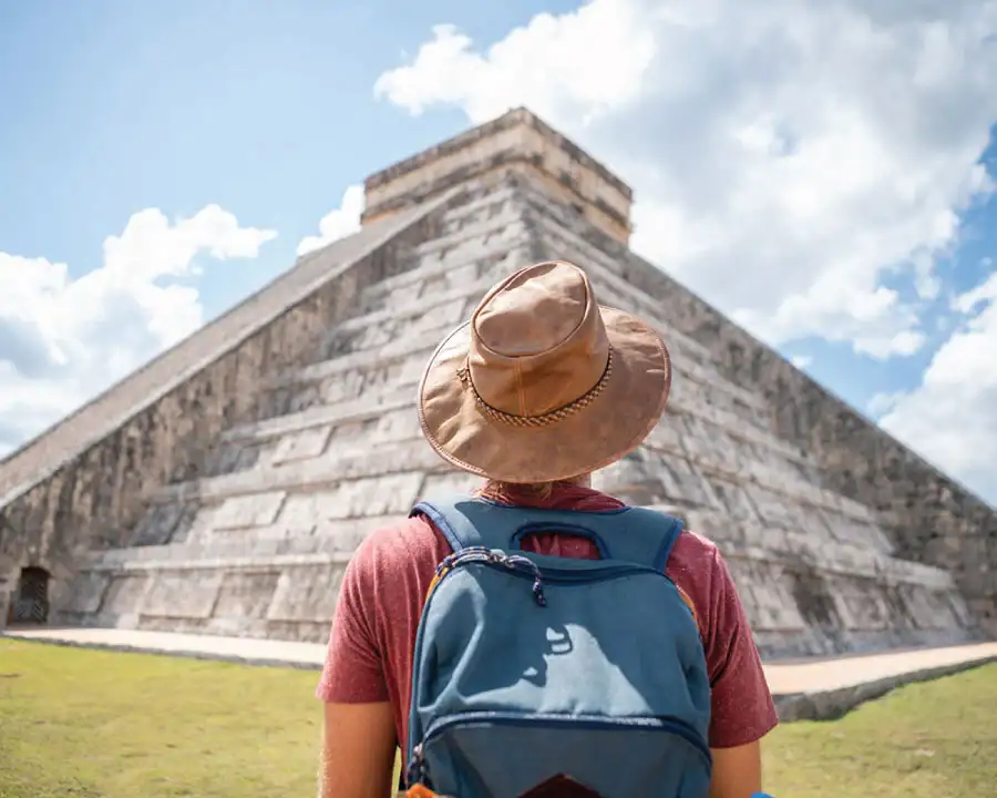 Person standing with their back to the camera, looking at the Chichen Itza pyramid on a sunny day.