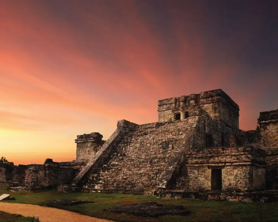 The pyramid called 'El Castillo' in Tulum, photographed at sunset with a sky filled with dark, orange, and purple colors, resembling flames.